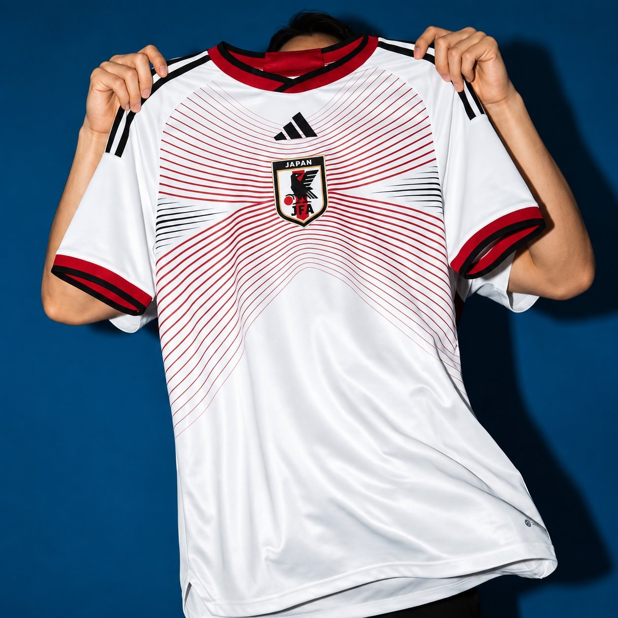 Japan retro home jersey in white with red radiating line pattern, held up against a blue background.