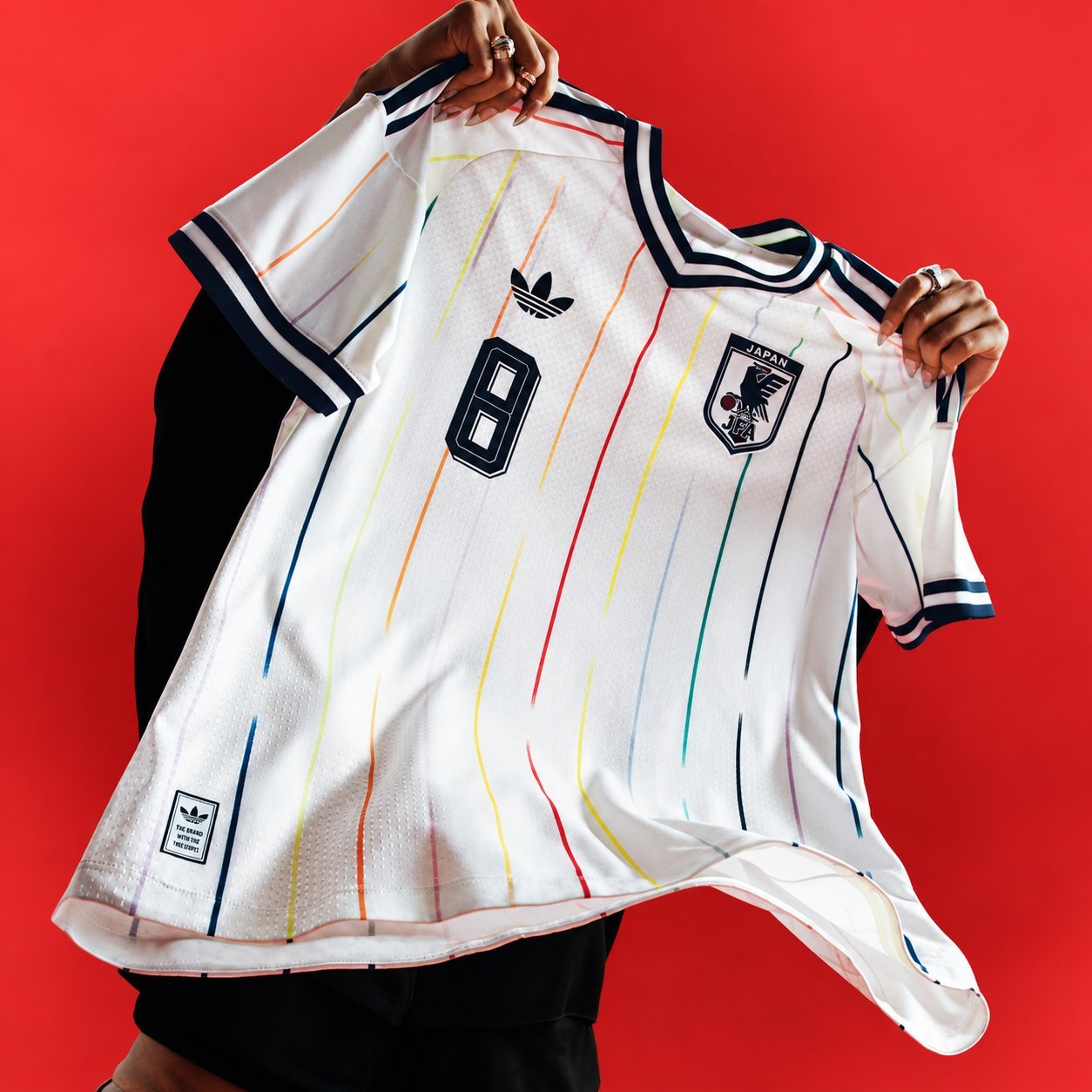 Japan retro away jersey in white with multicolored accent lines, held up against a red background.