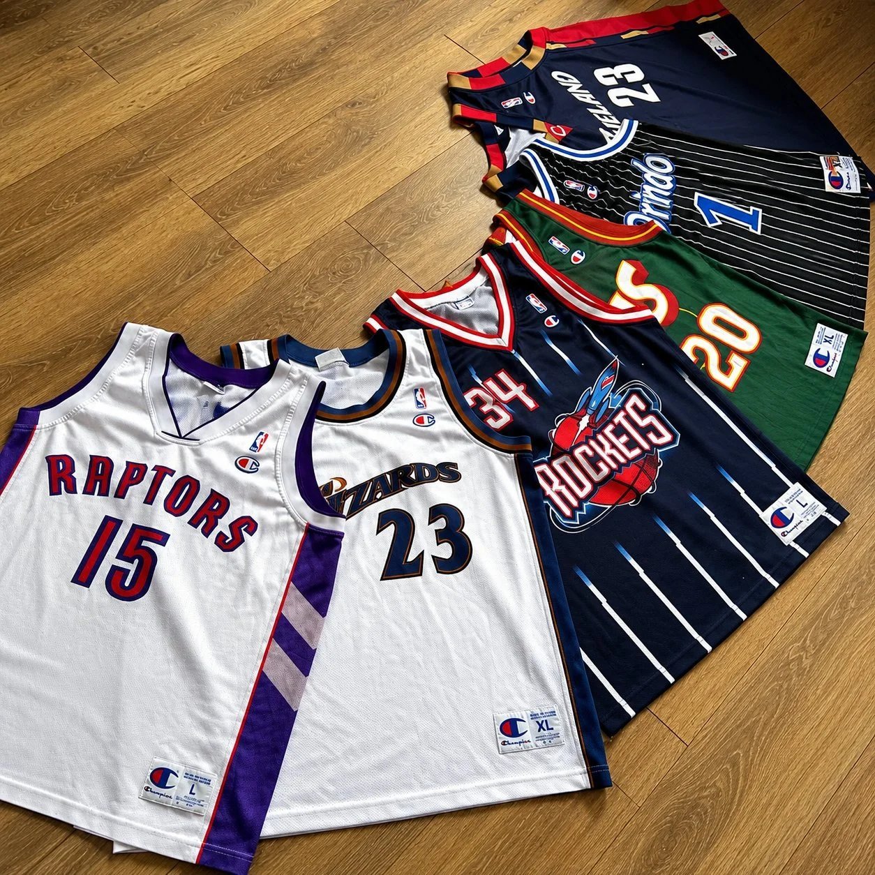 Eight retro NBA jerseys laid out including Raptors #15, Wizards #23, Rockets, Bucks, Cavaliers, Pacers and Hawks — full layout